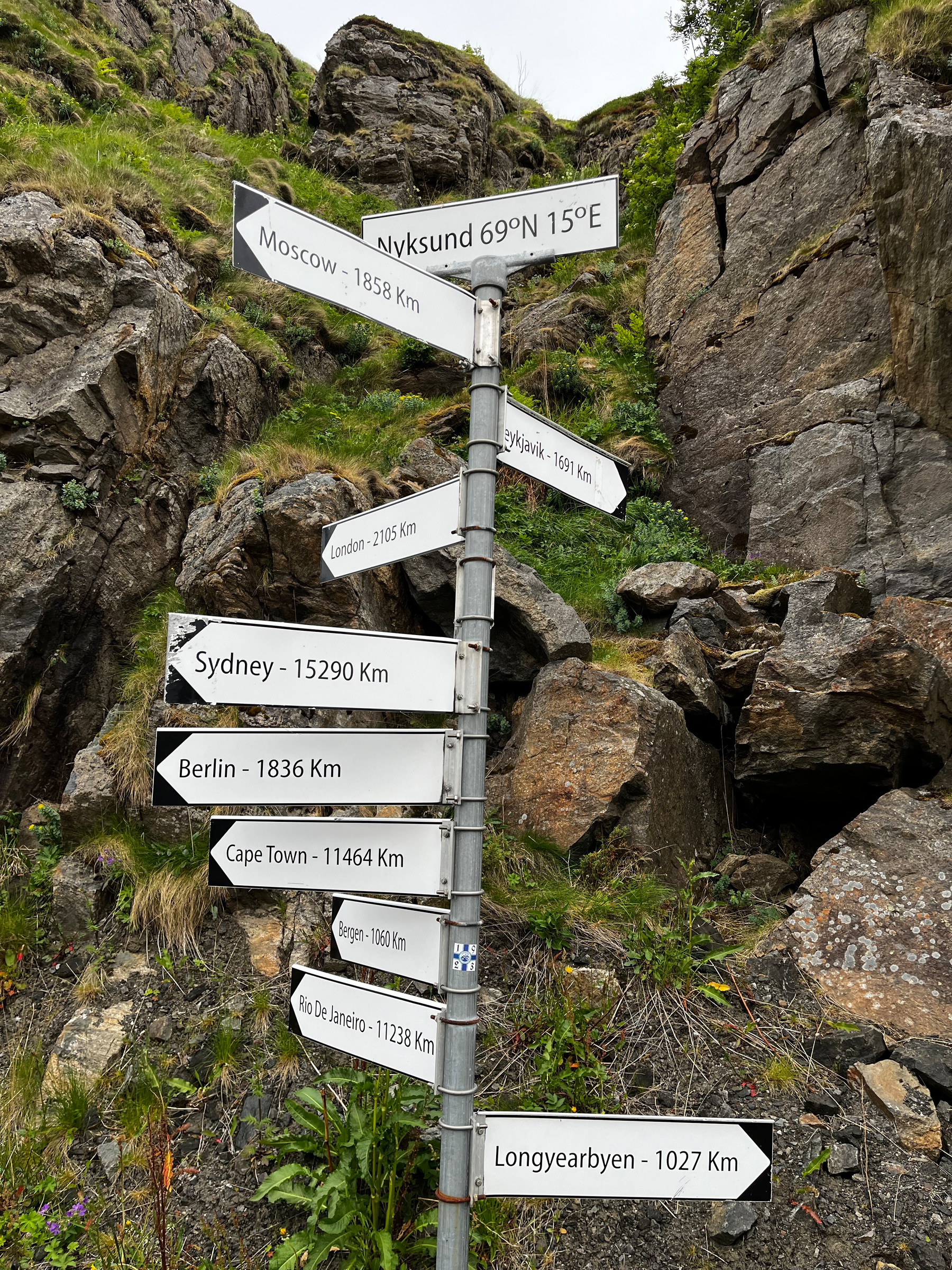 Ein Wegweiser mit verschiedenen Städten und Distanzen steht vor felsigem Hintergrund.