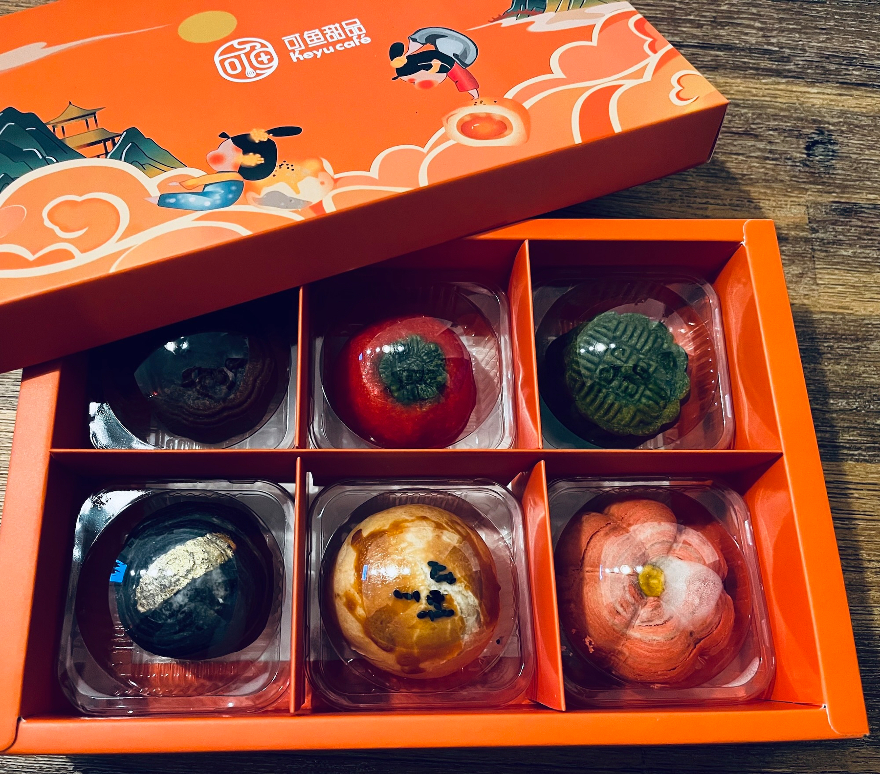 Eine Schachtel mit sechs kunstvoll gestalteten und in separaten Fächern eingelegten Gebäckstücken in verschiedenen Farben und Dekorationen.