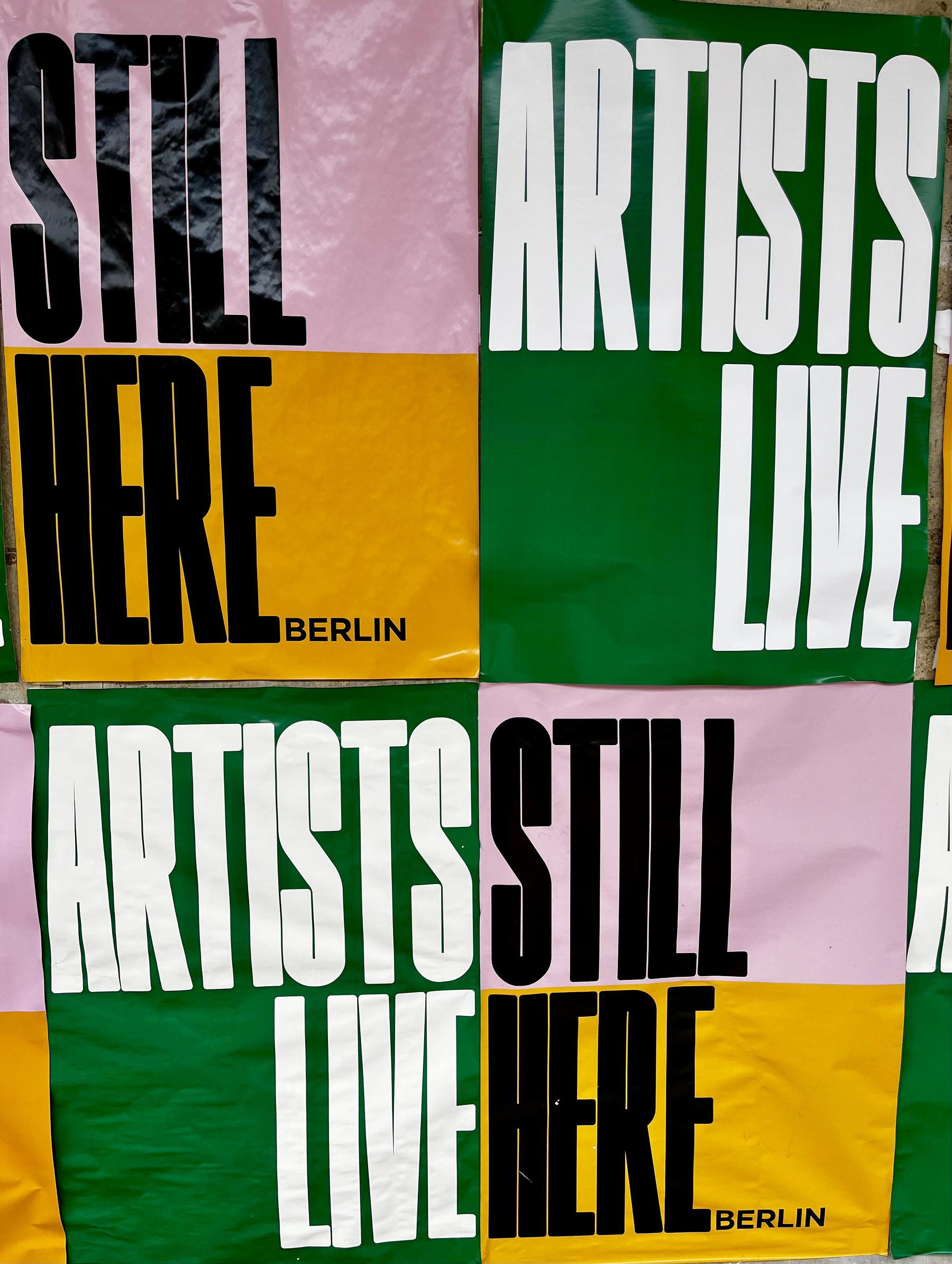 Plakate an der Wand eines Theaters mit auffälligen Farbblöcken und Schrift,  mit dem Text „Artists still live here“.